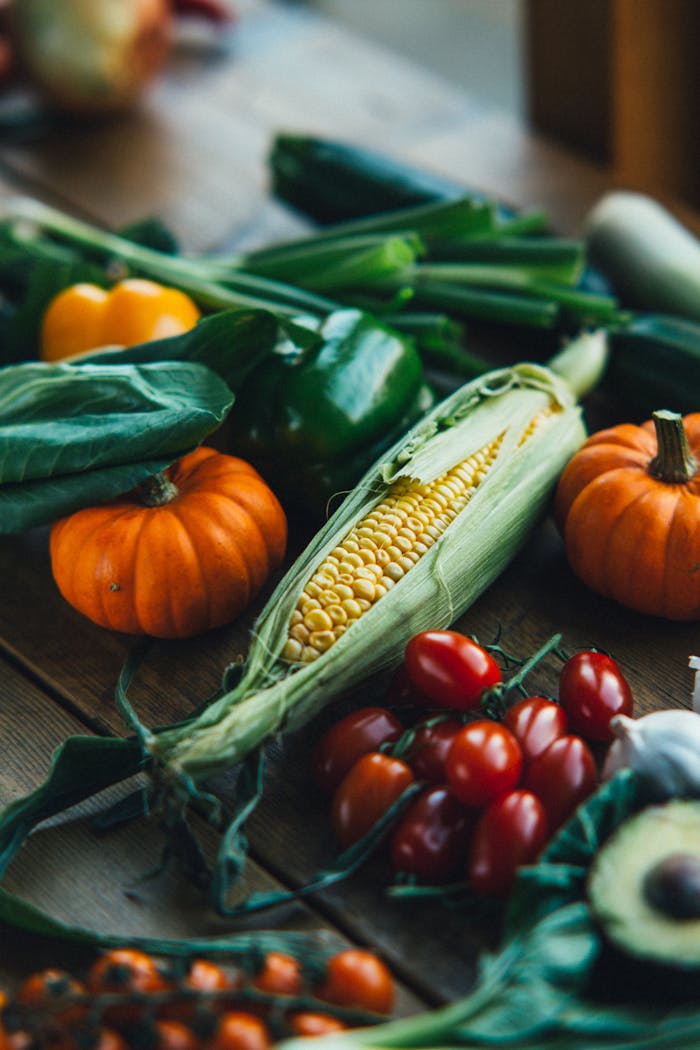 Vibrant display of pumpkins, corn, cherry tomatoes, and more on a rustic wooden table.